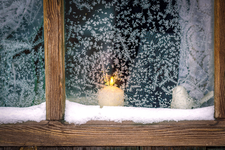 A wood-framed window, a frosty patterns. A candle burns outside the window.