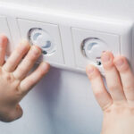 Two Child Hands Touching A Wall Socket With Safety Plugs to Prevent Child Hazard