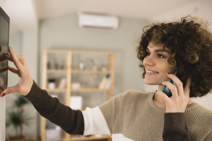 Young woman setting up the intelligent home system and talking on the phone.