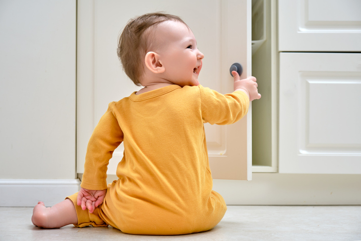 Toddler baby boy rips off a cabinet drawer with his hand. The child holds the cabinet door handle.