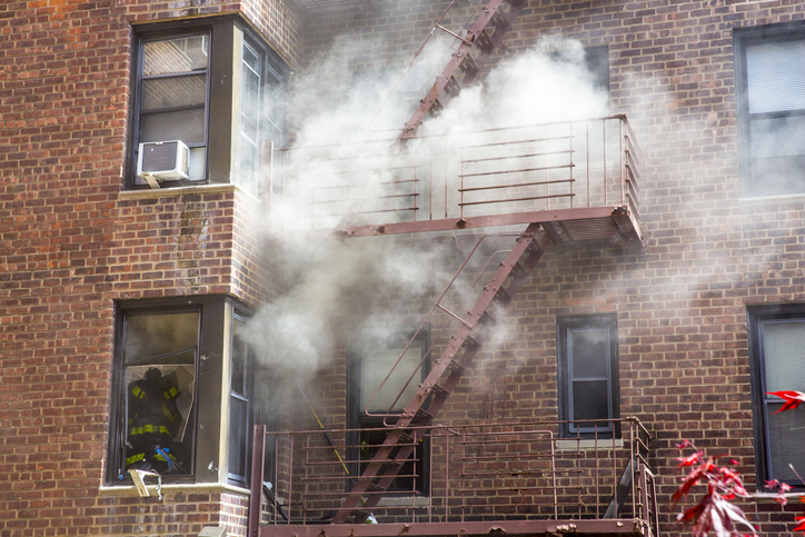 An old apartment is on fire with smoke coming out from the window.