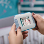 Caucasian female hands holding a baby monitor, with a crib background