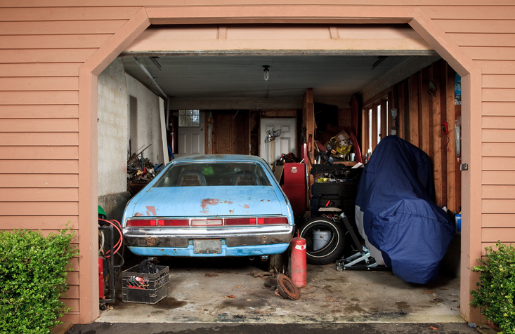 old blue car inside of a messy garage