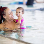 Mother teaching her baby daughter to swim in an indoor pool at a health club