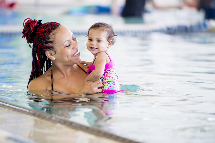 Mother teaching her baby daughter to swim in an indoor pool at a health club