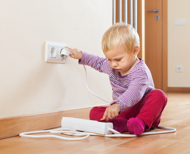 Baby playing with electrical extension on floor at home