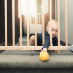 child playing behind safety gates in front of stairs at home