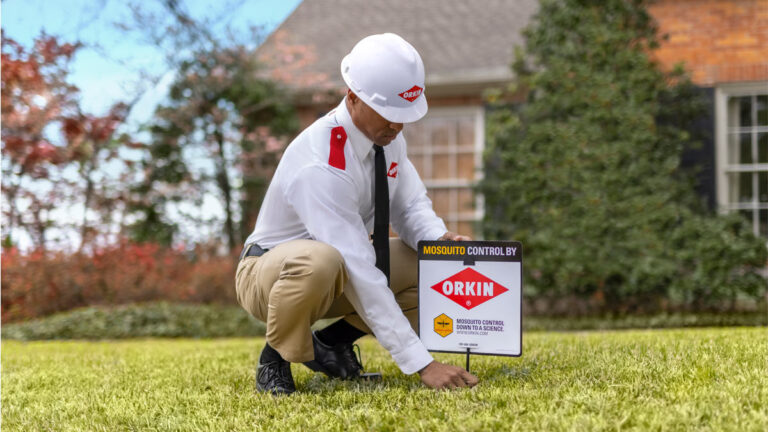 Orkin pro installing yard sign on healthy green lawn