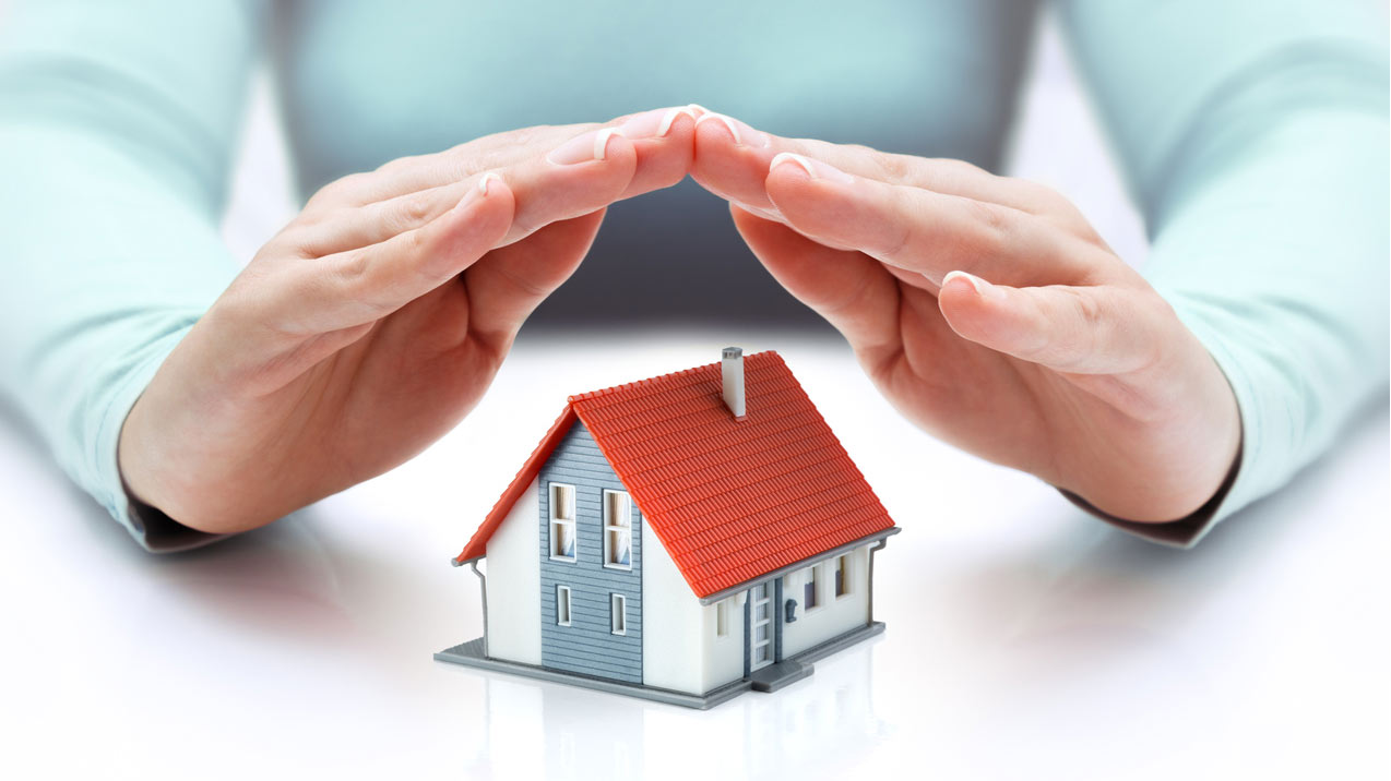 a shot that is used as the featured image of an article about home warranties. A person holding his hands protecting a small model of a home on a table